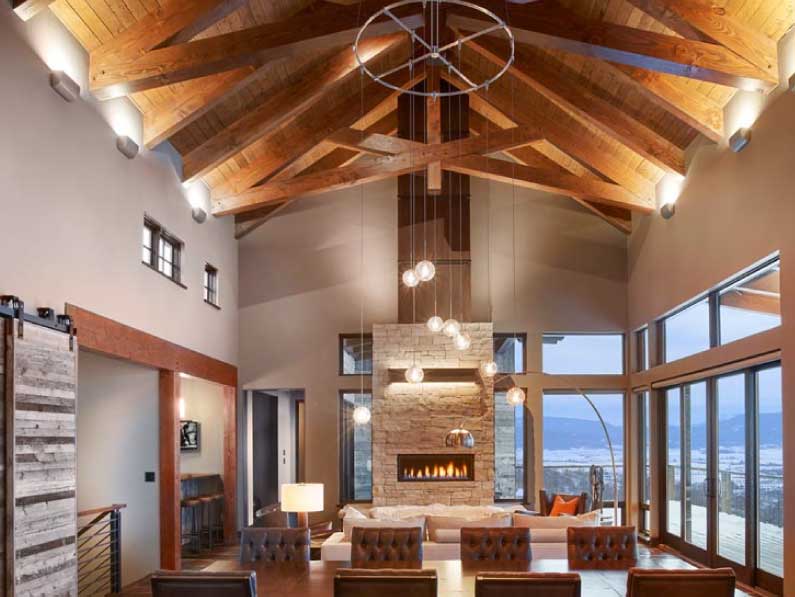 A spacious living room with high wooden ceilings, exposed beams, and a stone fireplace. modern furnishings are complemented by large windows offering scenic views.