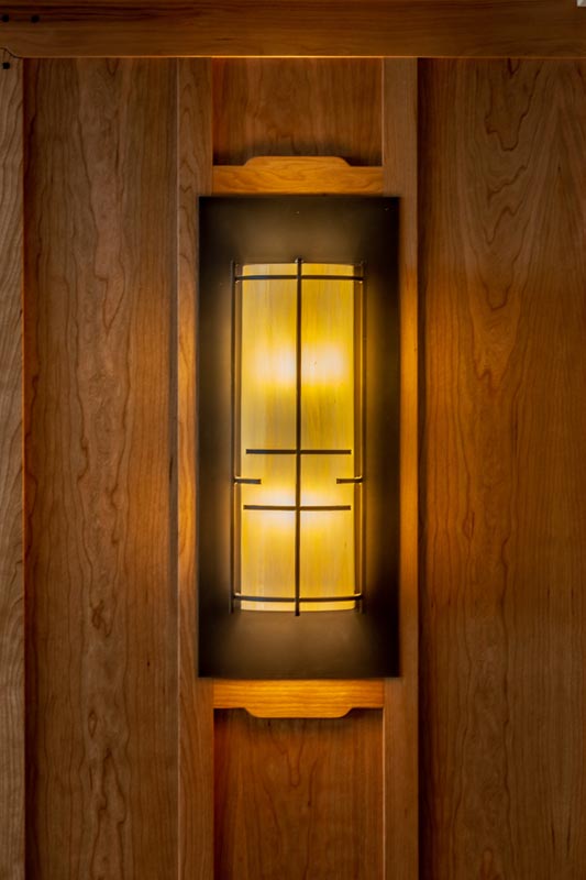 A warmly lit, rectangular lantern set into a wooden wall panel with vertical grain, providing a calming, indirect lighting effect.